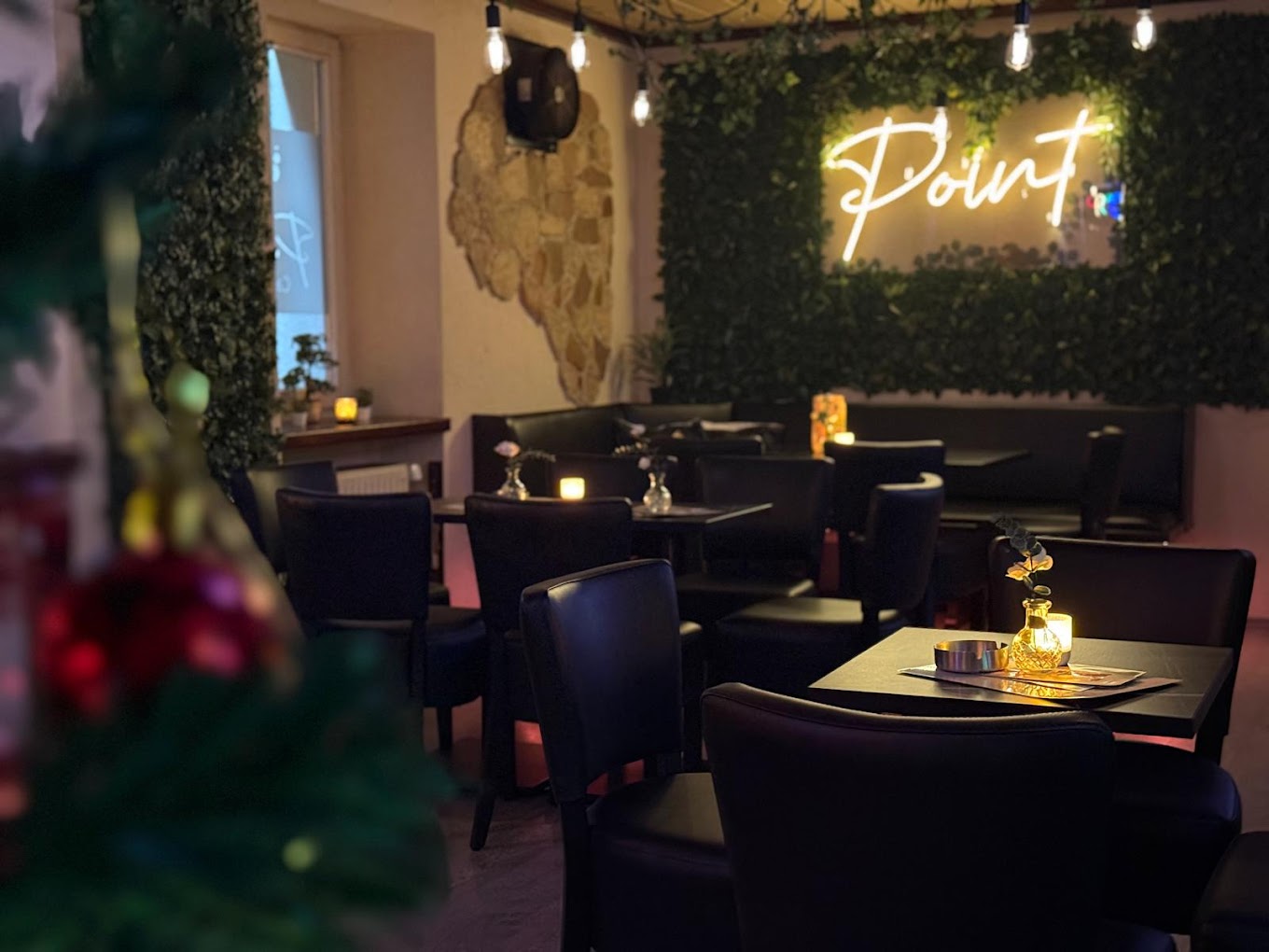 Gemütliches Kerzenlicht-Ambiente im Point Cafe Bar mit Point-Neonschrift und Efeu-Wand